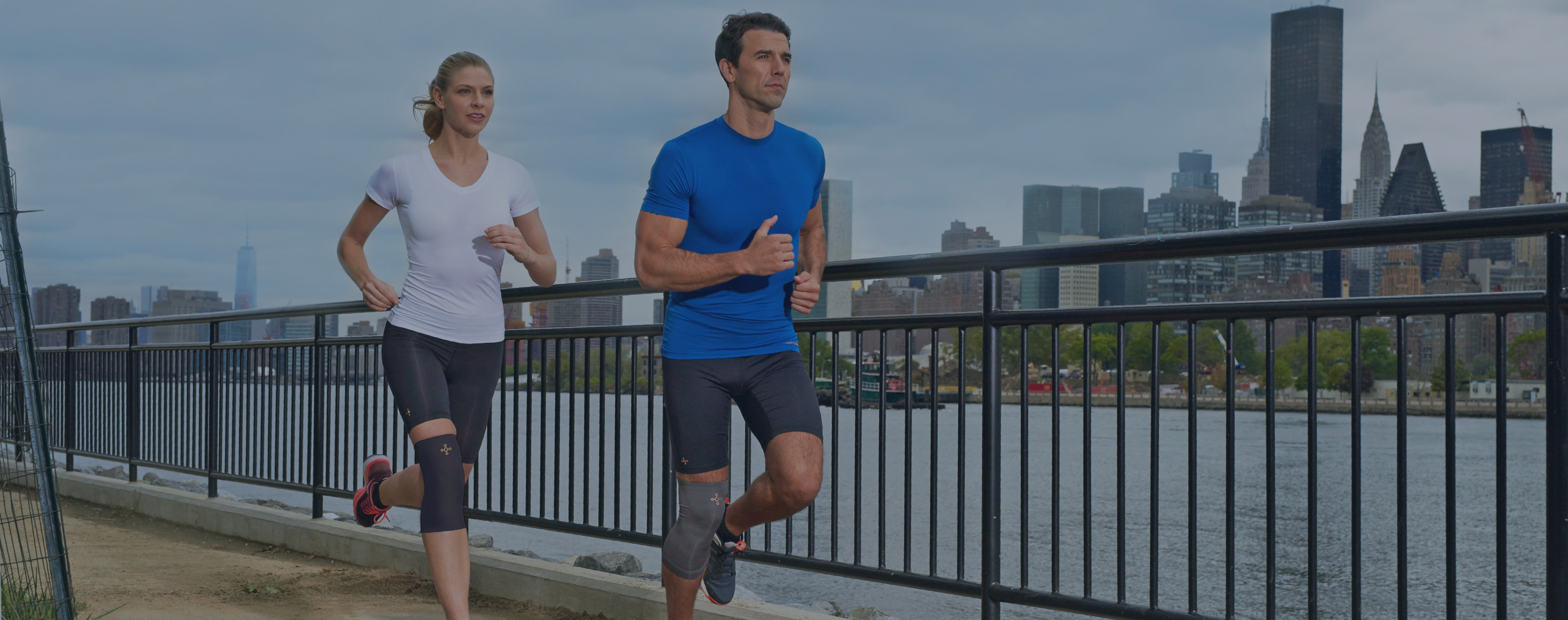 Two people jogging along a river path wearing Tommie Copper compression