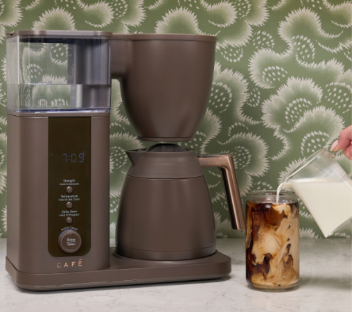 Coffee maker pouring milk into a glass of iced coffee.