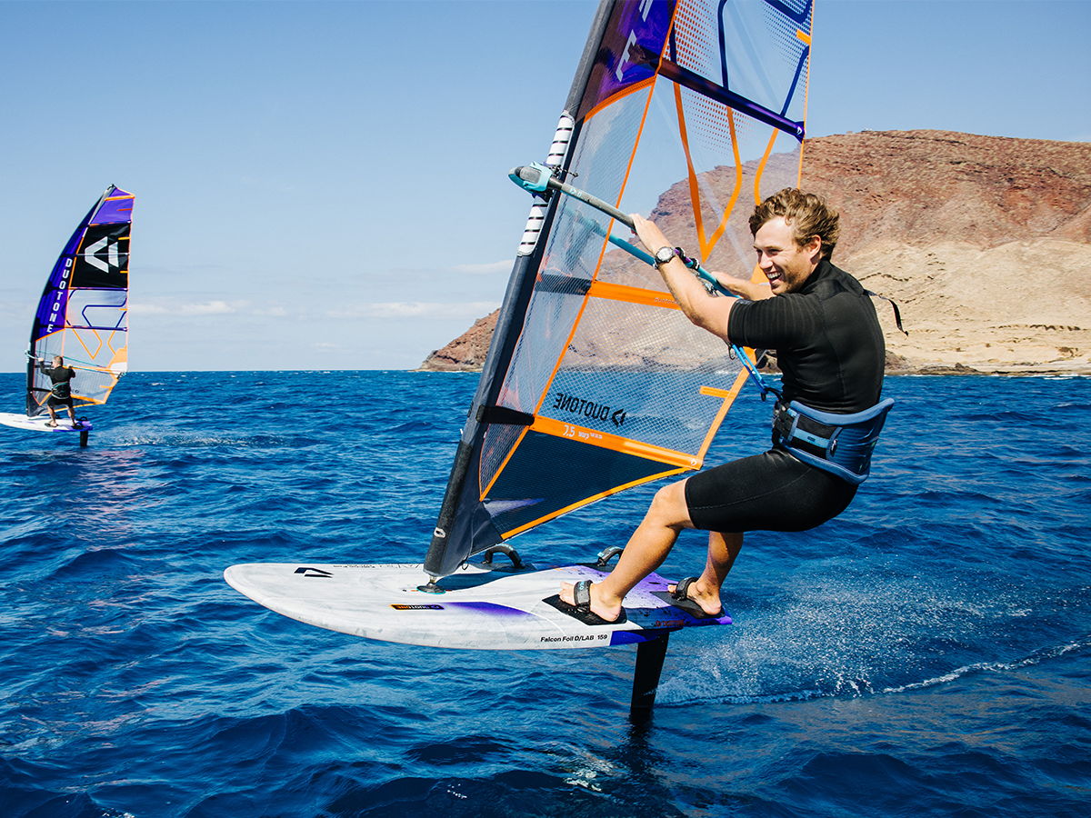 Person windsurfing on water with mountains in the background.