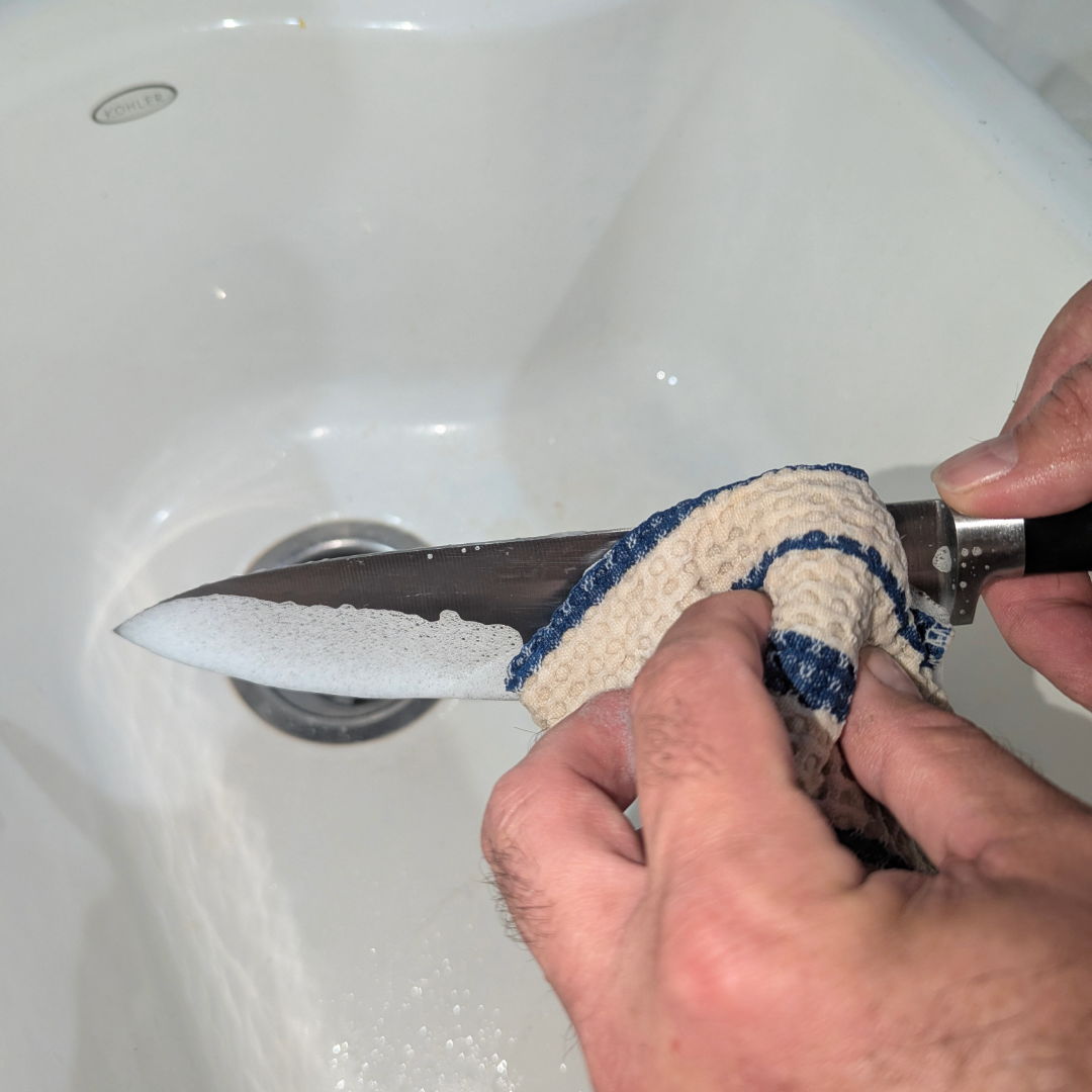 Person cleaning a knife over a sink.