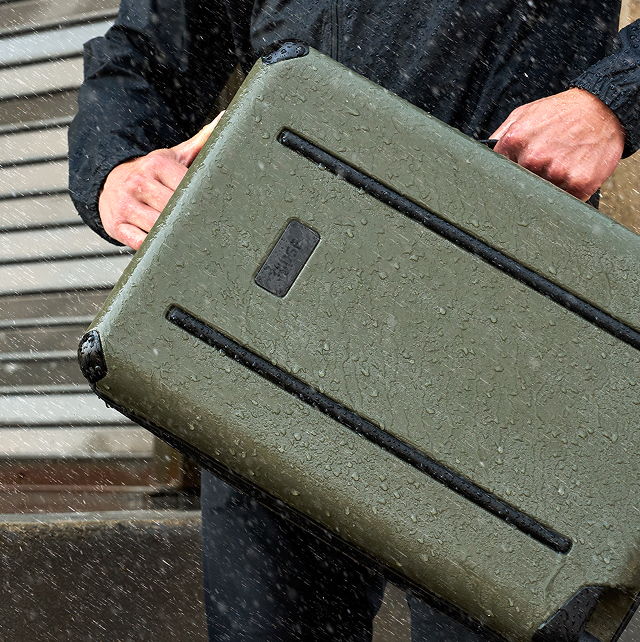 Person holding a waterproof green suitcase in the rain.