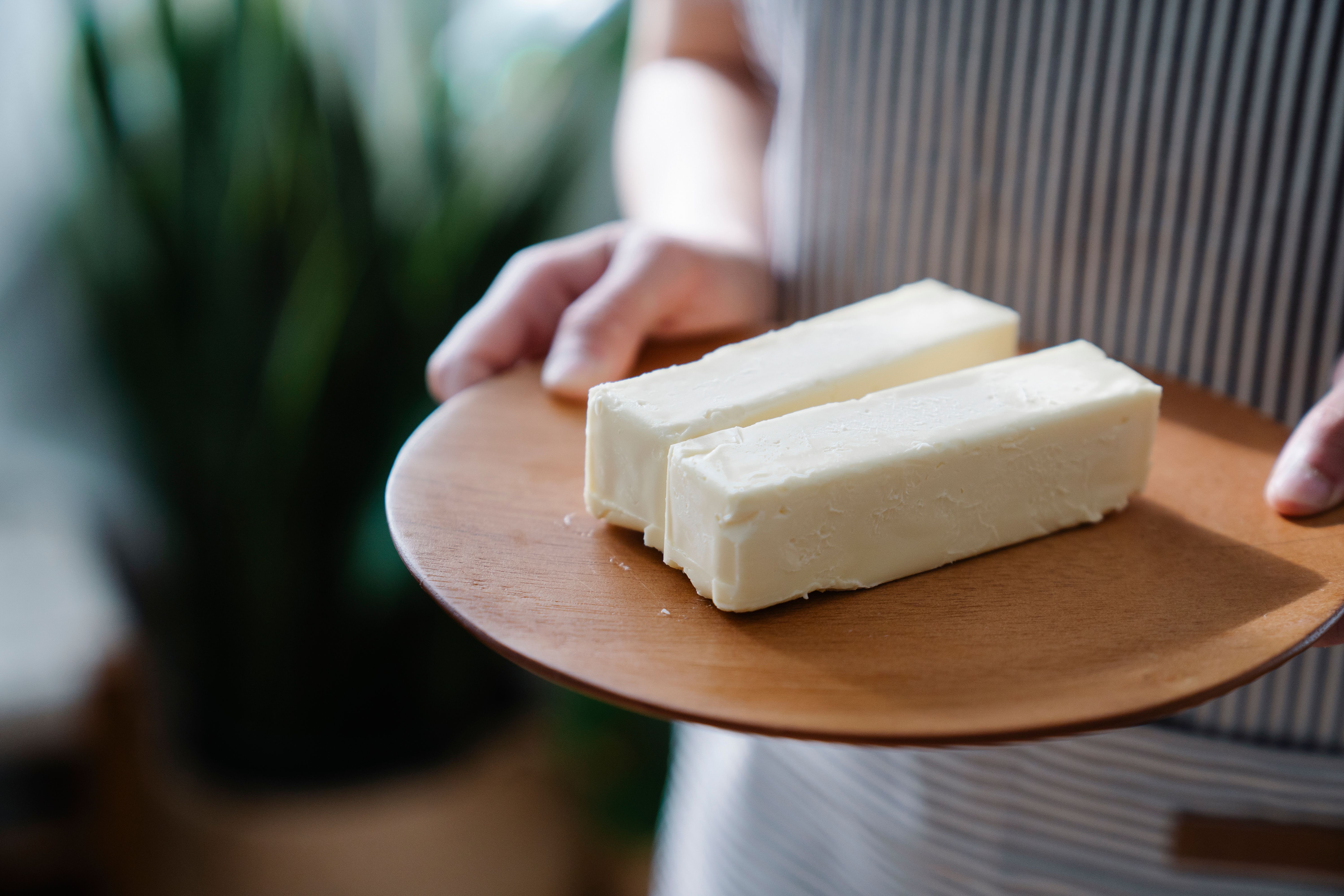 Person holding a wooden plate with two sticks of Beef Tallow