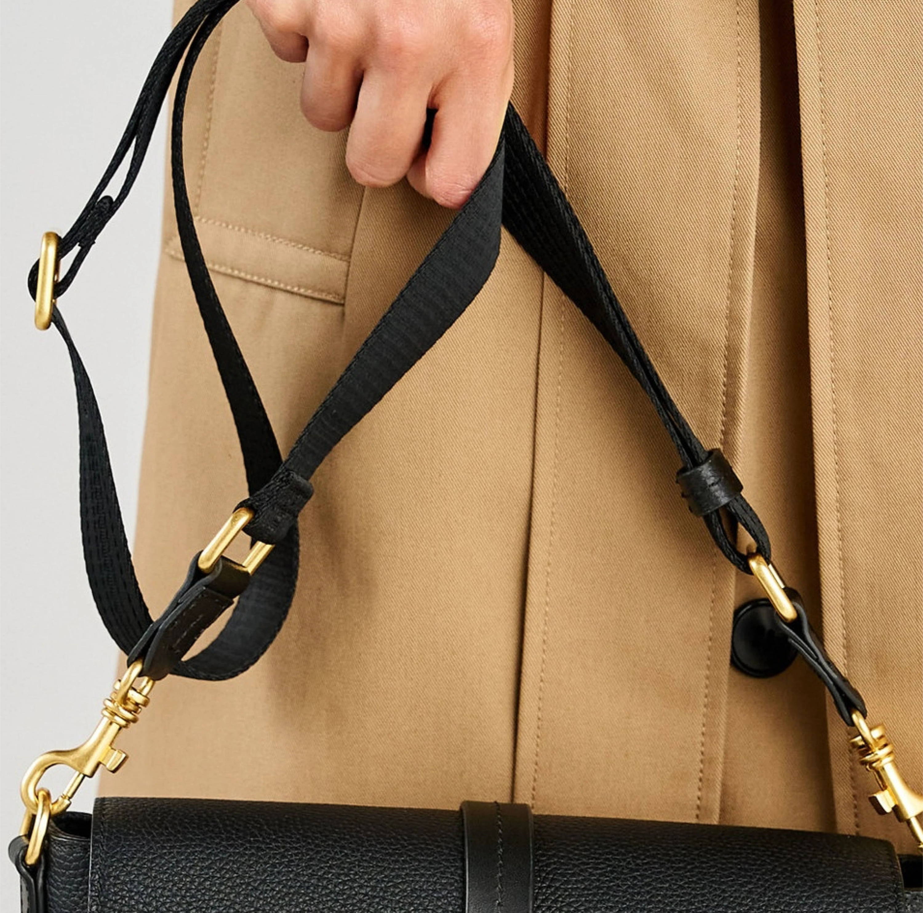 A hand holding a black handbag with a gold strap.