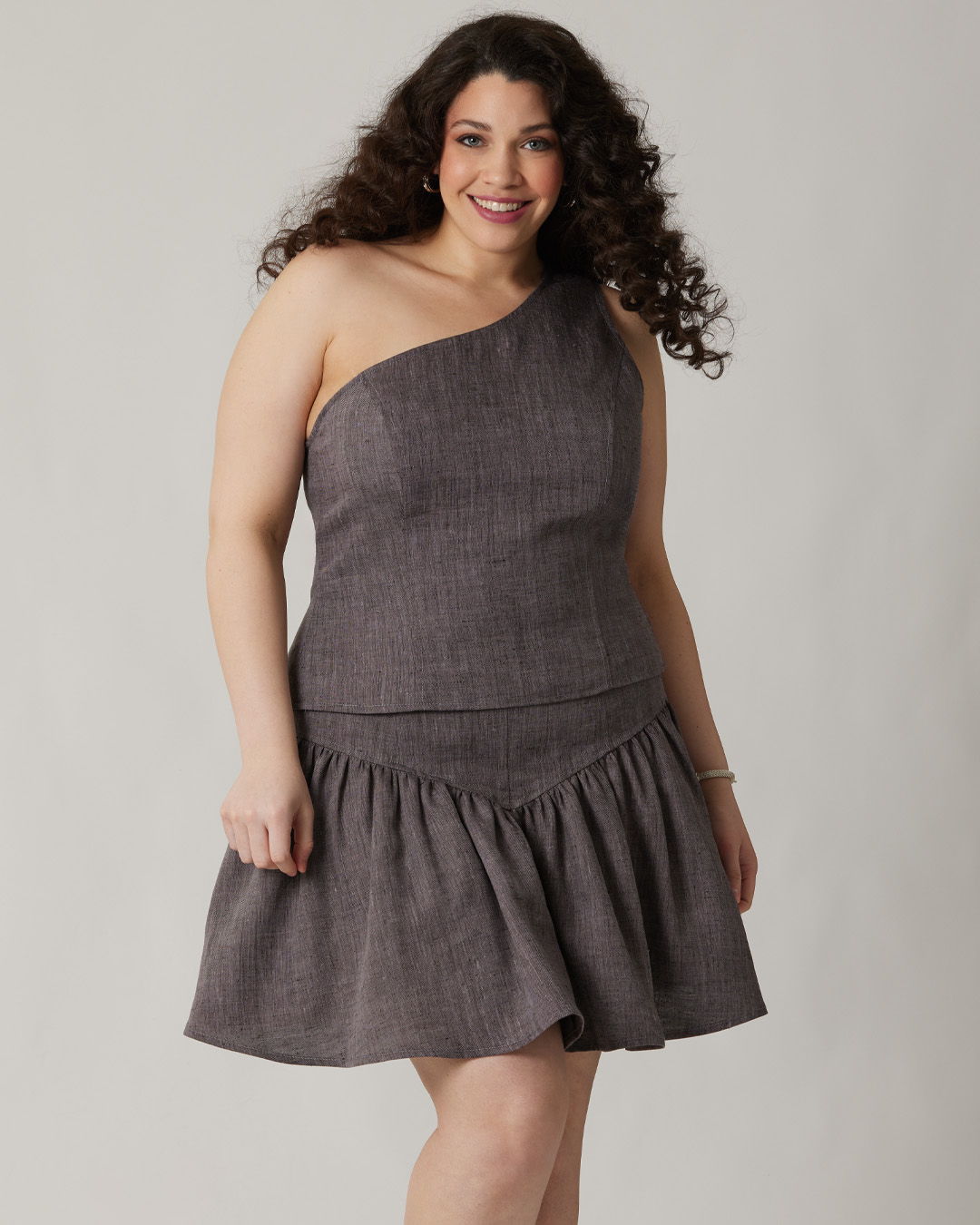 A woman in a one-shoulder gray dress smiling at the camera.