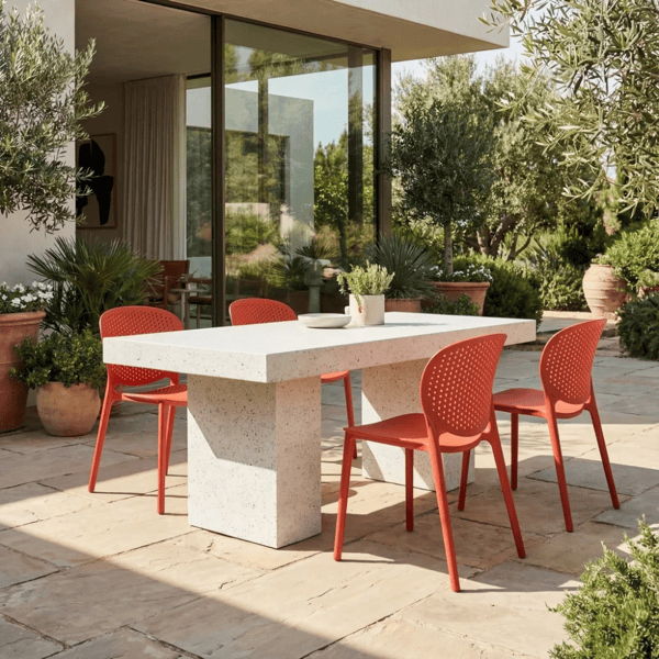 Outdoor lounge seating arranged around a square concrete fire pit on a desert patio, with cushioned club chairs and a market umbrella.