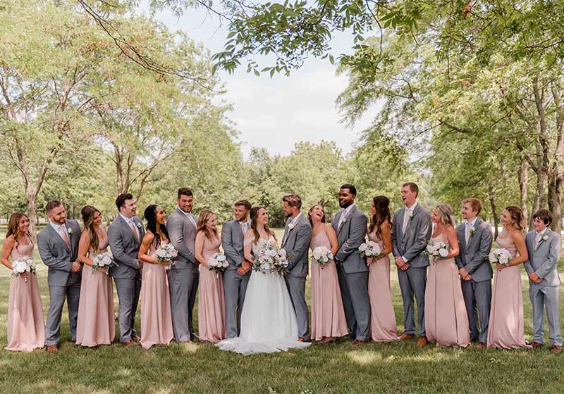A large wedding party wearing shades of blush pink and gray outside