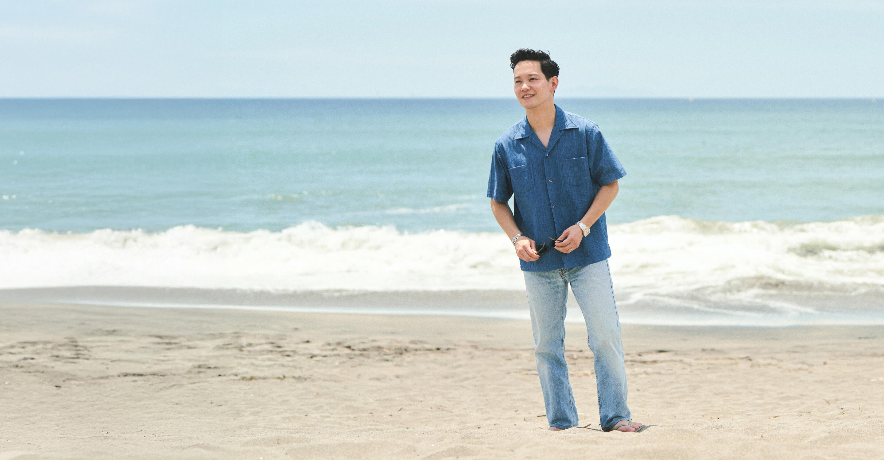 Person standing on a beach with ocean waves in the background.