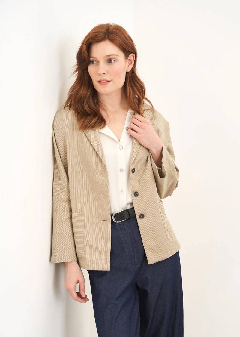 A model wearing a beige and khaki stripe boxy jacket over an off white top with blue jeans