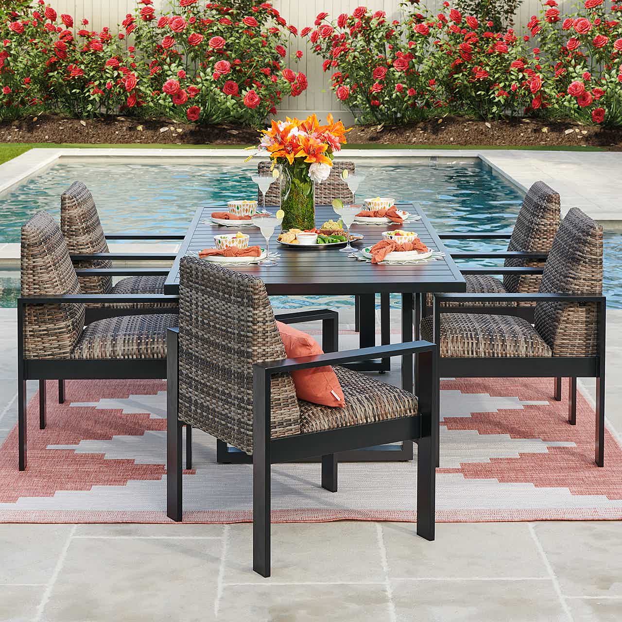 Outdoor dining table set by a pool with flowers and chairs.