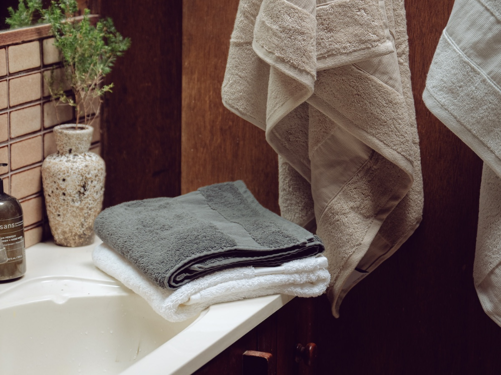 a grey and white hand towel stacked on the side of a bathroom sink 