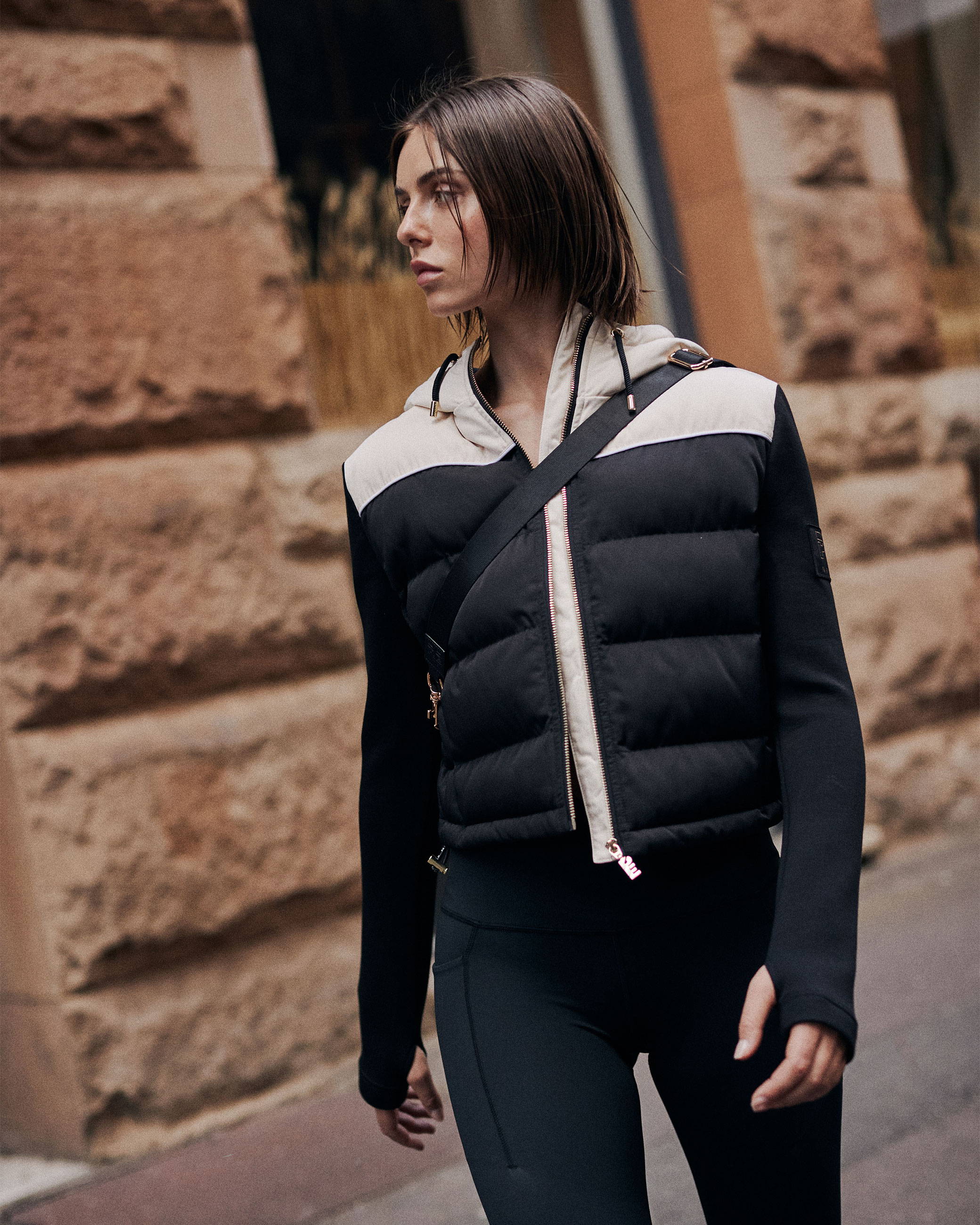 A girl is walking down a city street wearing activewear, a black and white jacket and a cross body bag, her look is active but elevated
