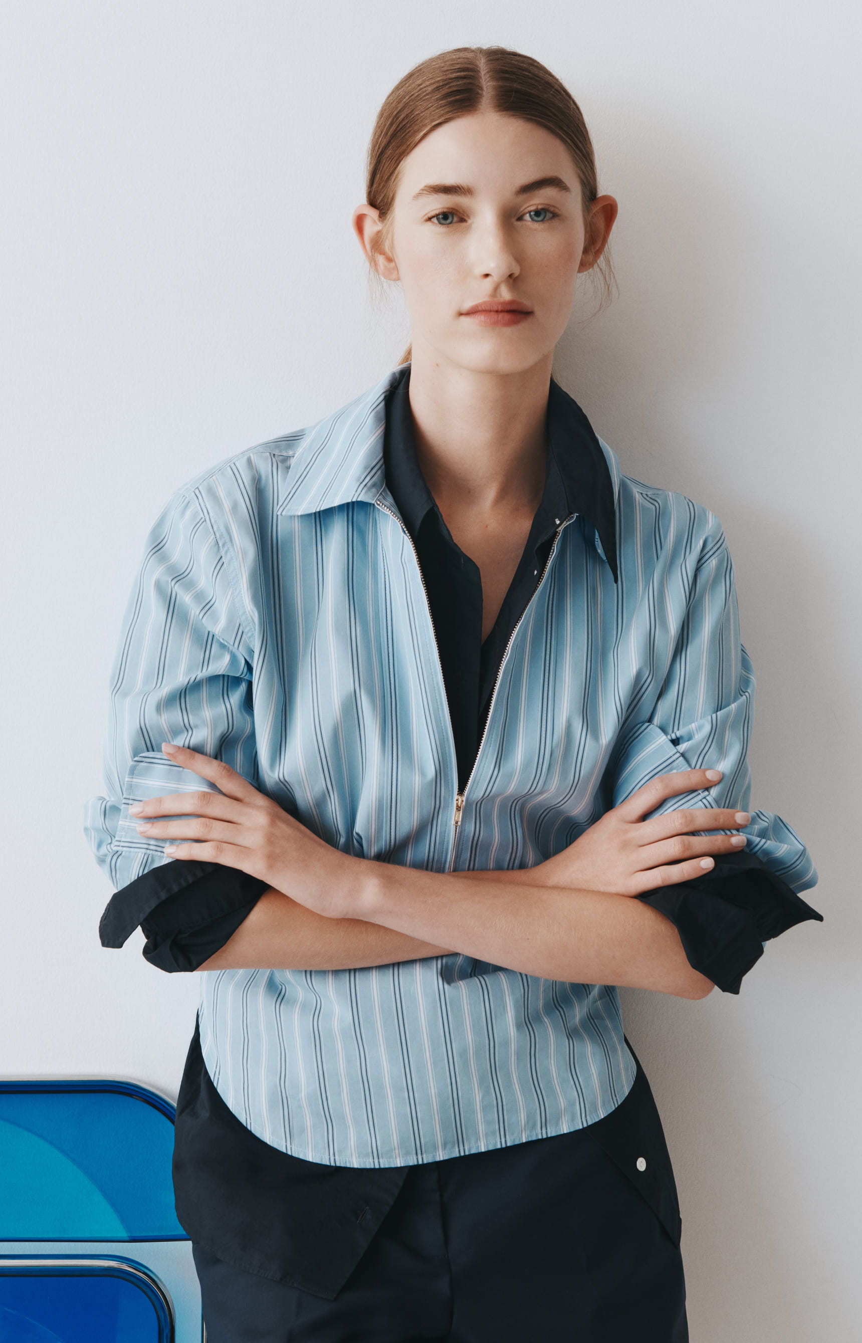 A woman in a blue striped shirt poses with arms crossed.