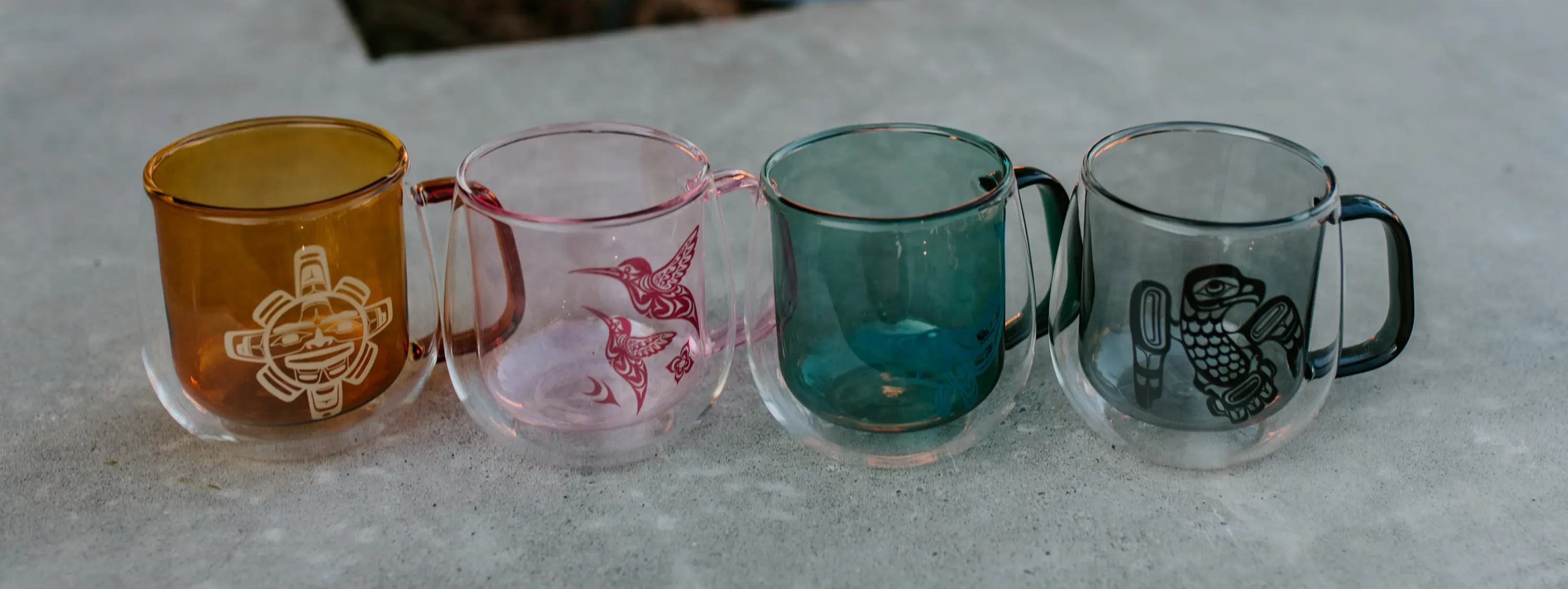 Double Walled Coloured Glass Mugs featuring Indigenous artwork — amber, pink, teal and dark glass — Native Northwest