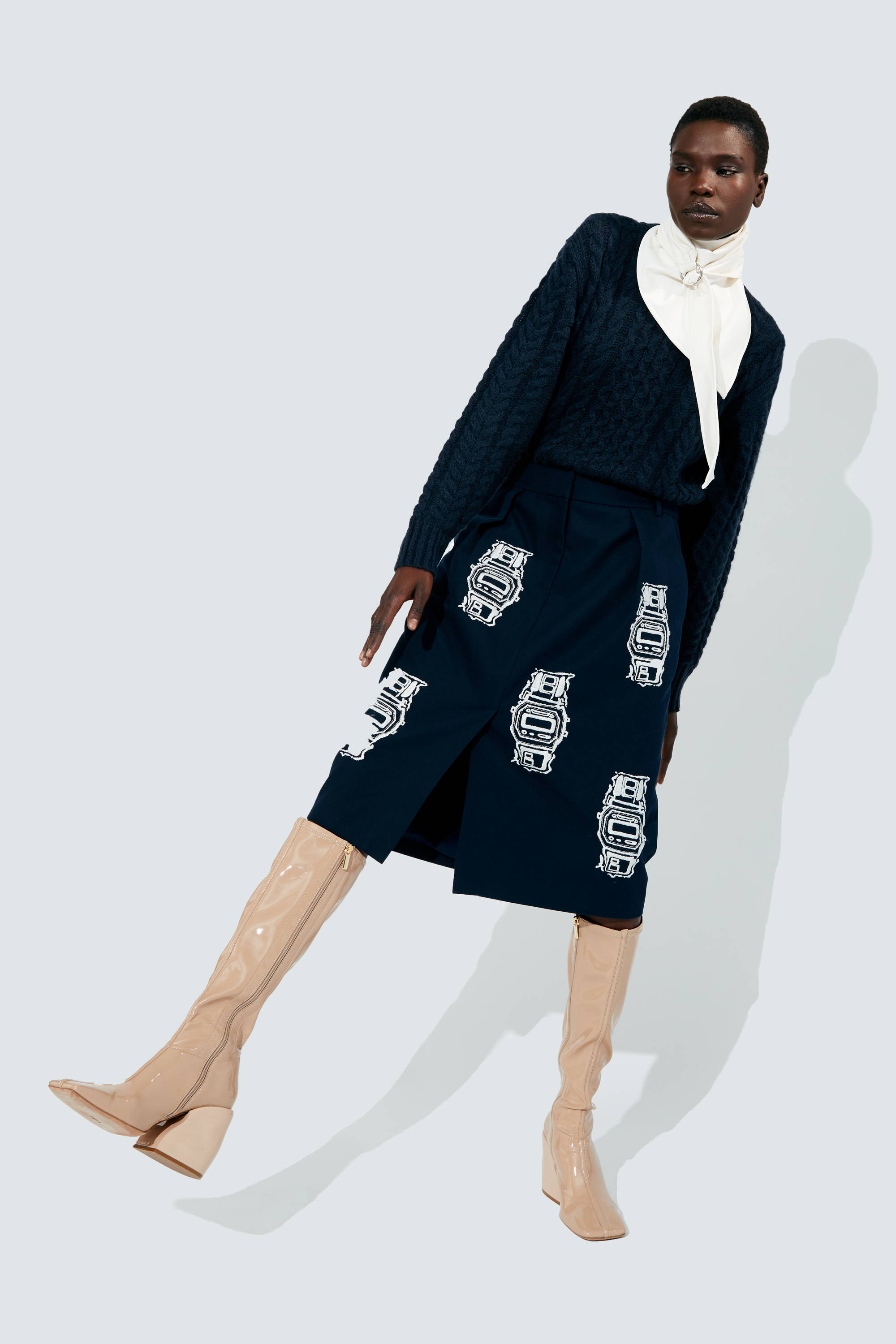 Model wearing navy outfit with white accents and beige knee-high boots.