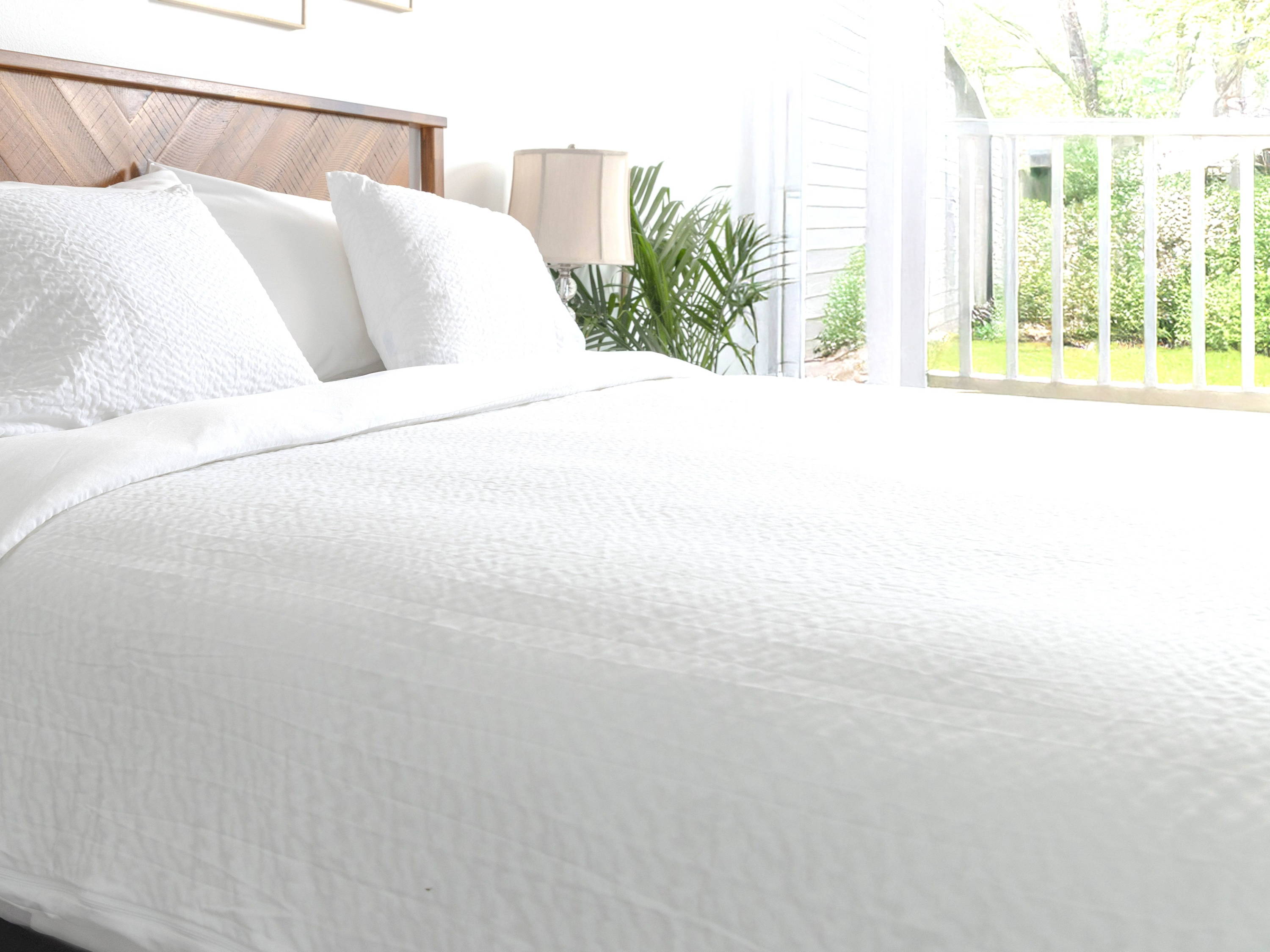 Bed in a sunny room witn brown wood headboard, dressed with comfortCore bedding - cumulus duvet cover and twill - in front of a window to a garden 