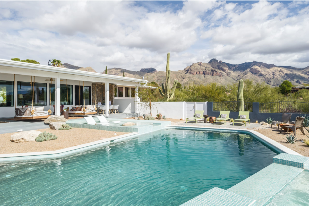 A modern desert pool deck with teal tile, green chaise lounge chairs, in pool tanning shelf, and a view of the mountains