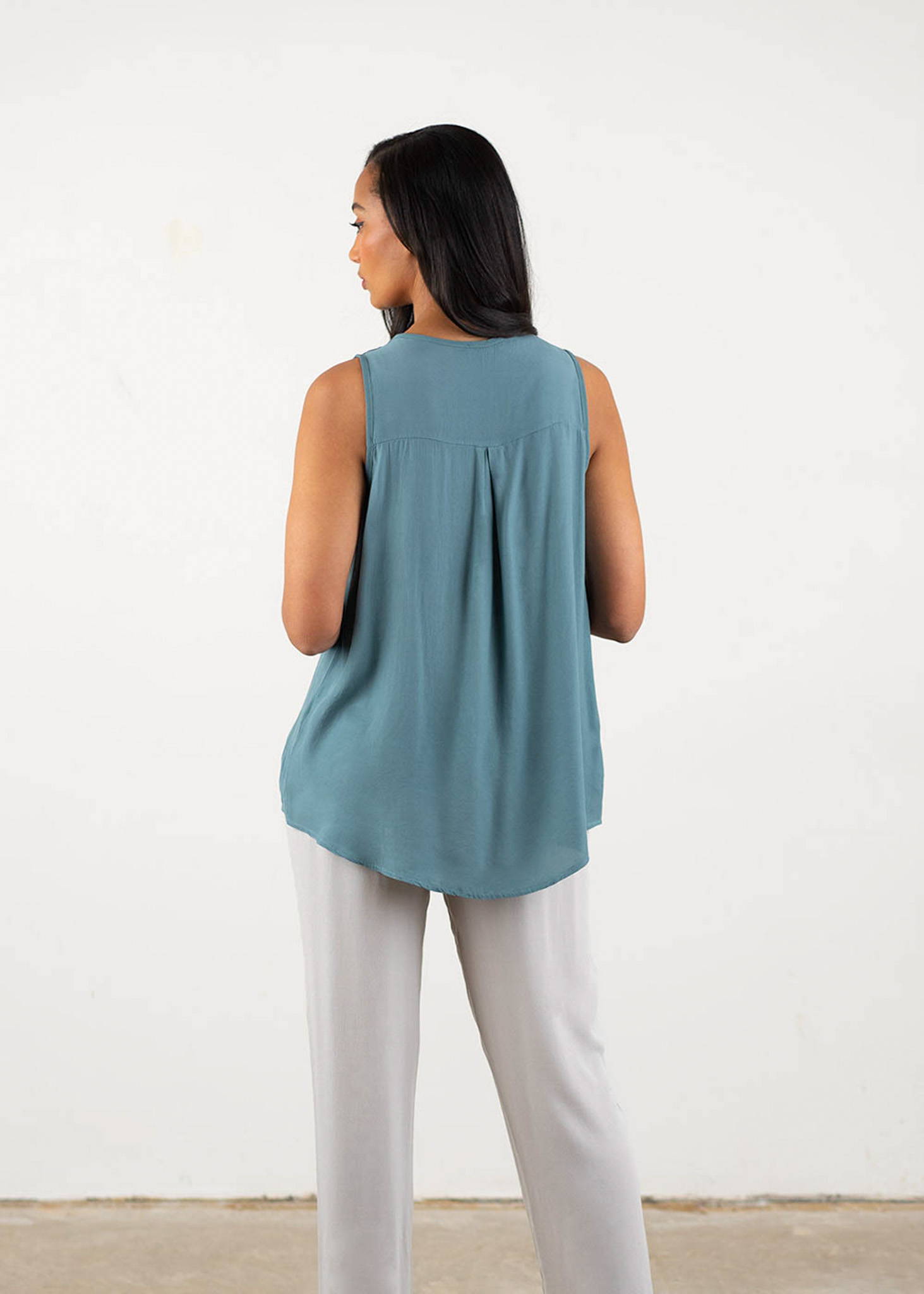 A model wearing a blue grey v-neck, sleeveless top over oatmeal drapey trouser and cream block heels