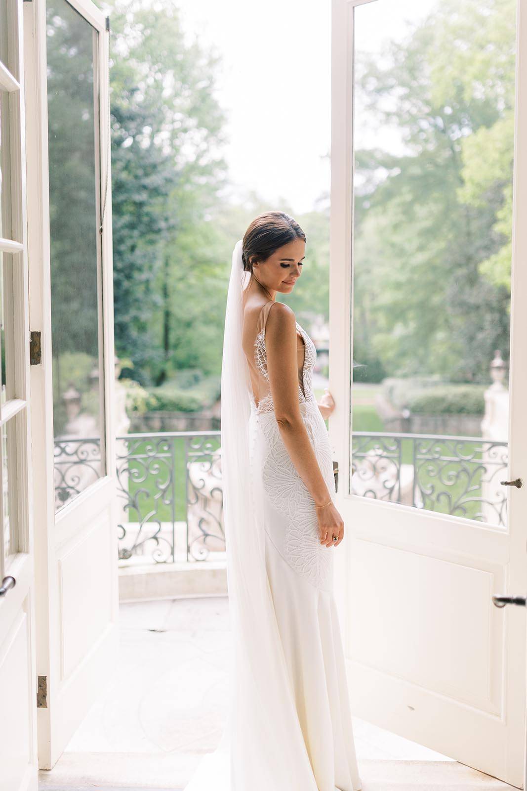 Beautiful bride stands in front of a beautiful balcony backdrop, beaming with joy as she showcases her bridal attire.