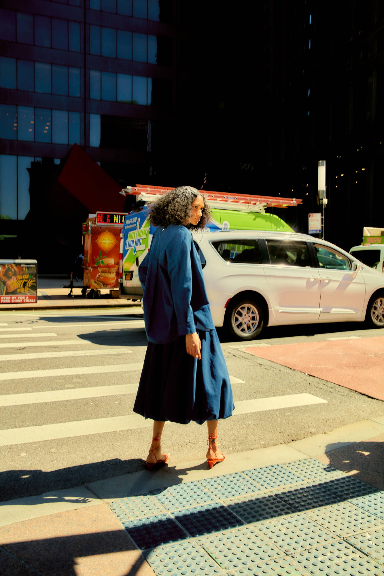 Person in blue outfit crossing a street with vehicles in the background.