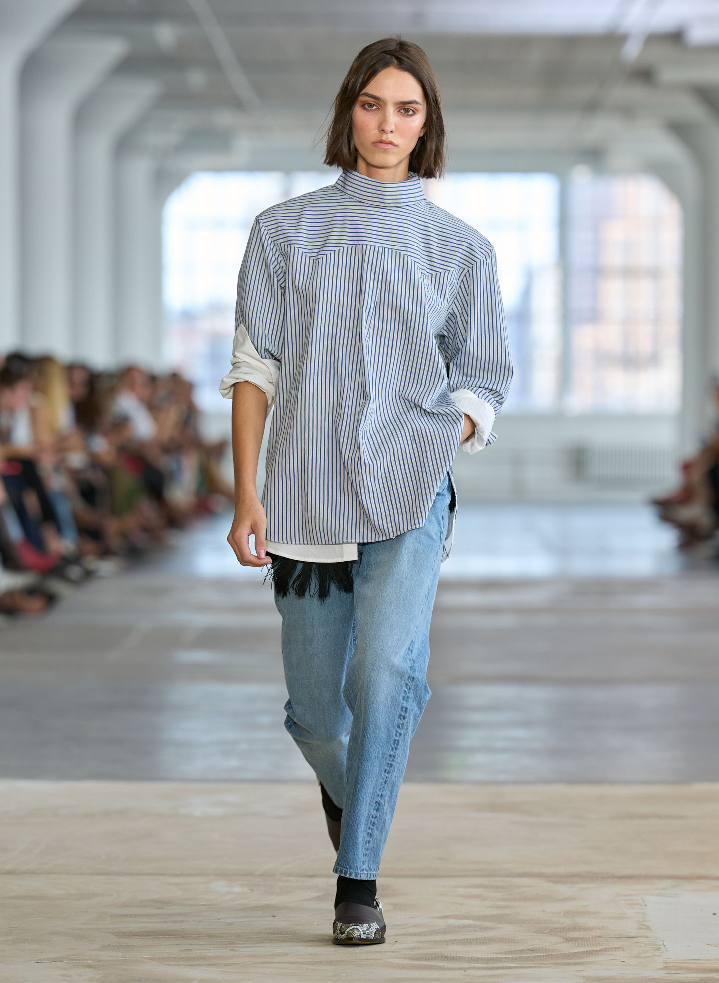 Model walking on runway in casual outfit during fashion show.