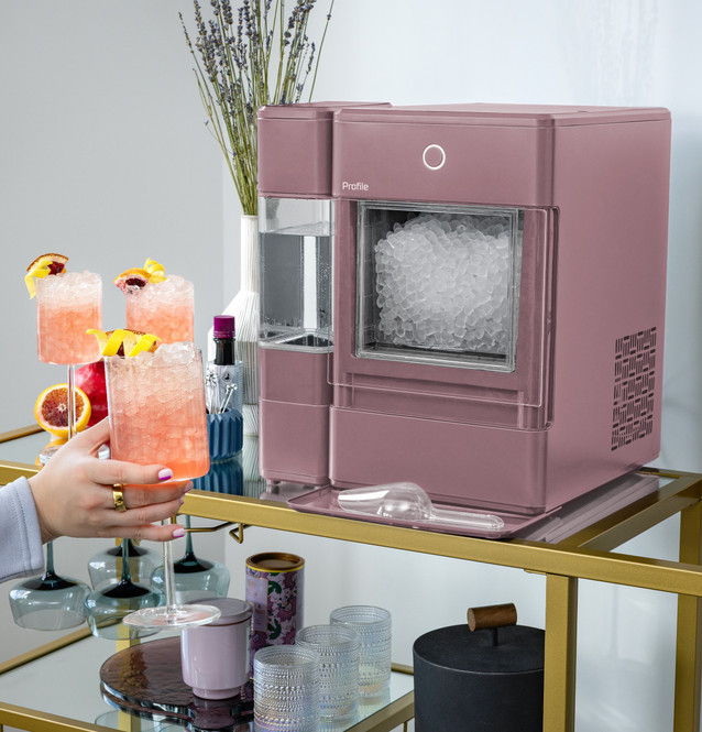 A pink ice maker on a bar cart with cocktails and decorative items.