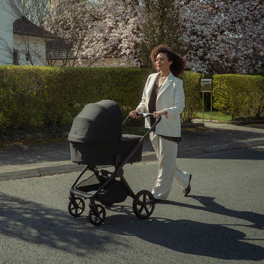 Woman in a suit pushing a stroller on a sunny sidewalk.