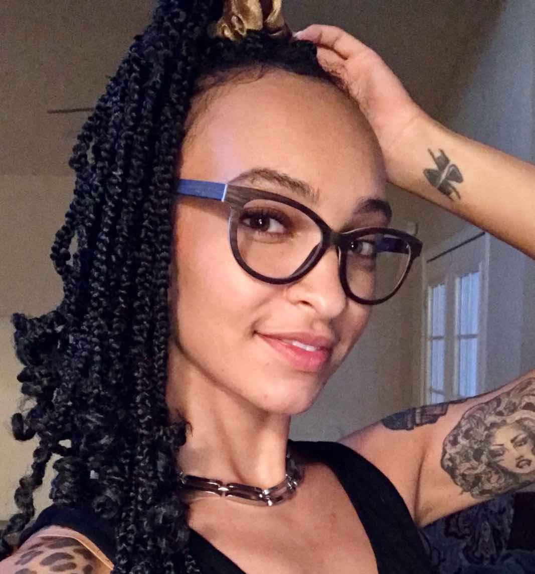 Woman with Big nose wearing Charm Purple, Cat-Eye Eyeglasses made from Sandal Wood with arm tattoos, a black shirt and silver necklace