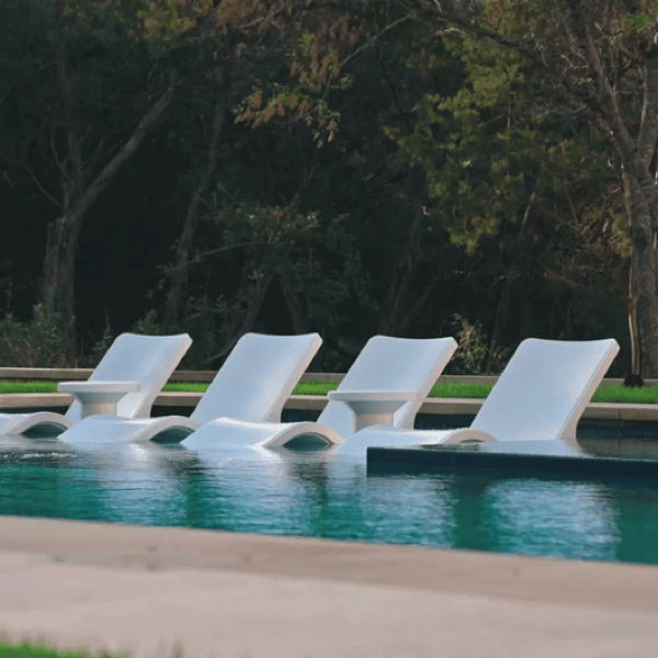 White in-pool chaise lounges arranged on a tanning ledge in a modern swimming pool, designed for resort-style outdoor lounging.