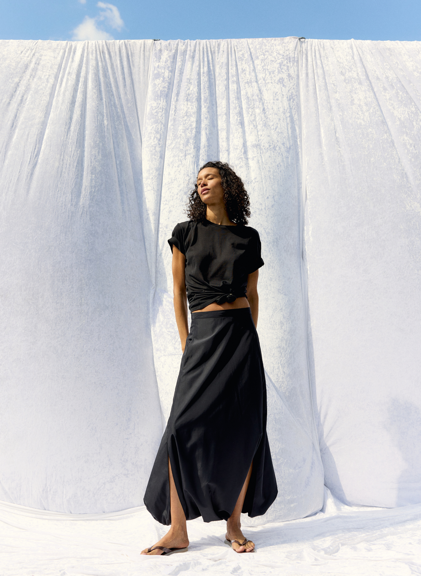 Woman in black outfit standing against a white backdrop.