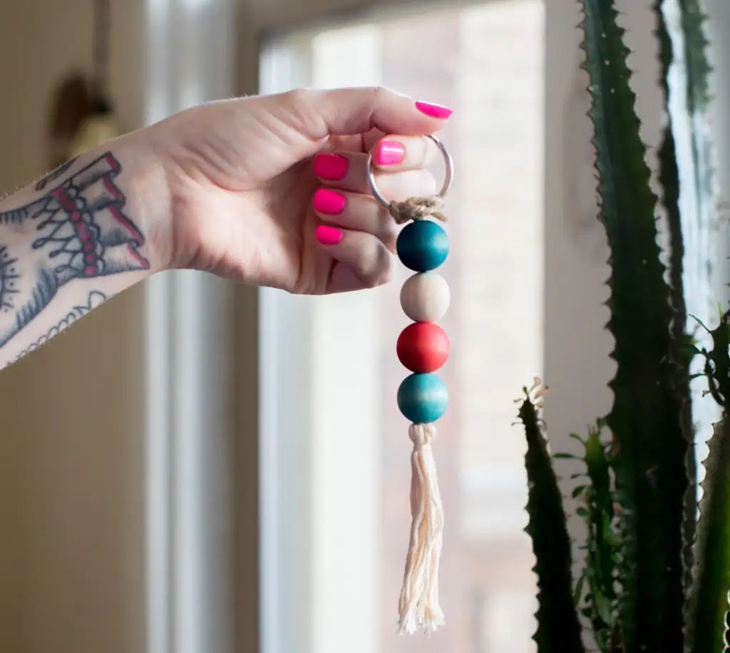 Hand holding a colorful keychain near a window with a plant.