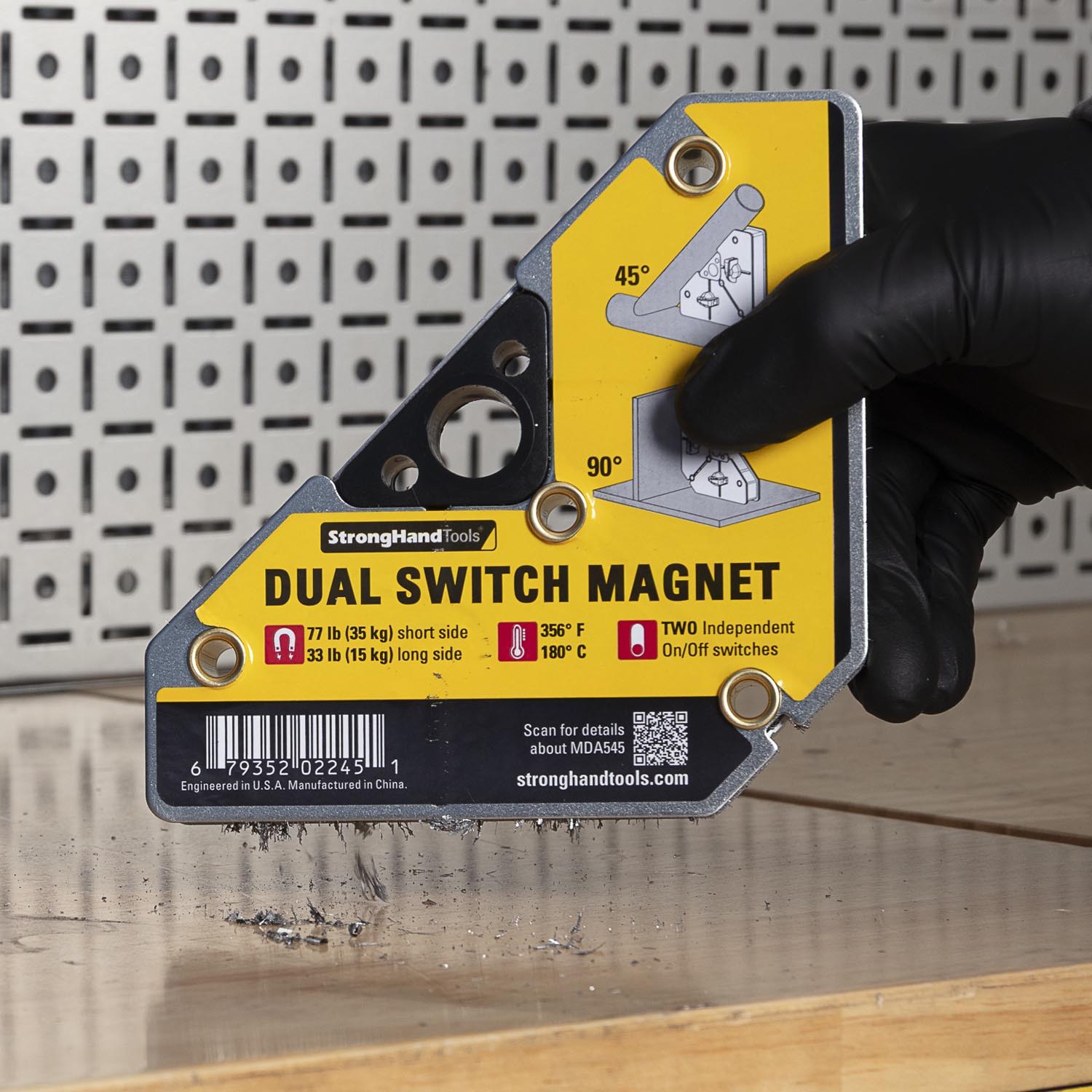 A hand holding a dual switch magnet tool on a wooden surface.