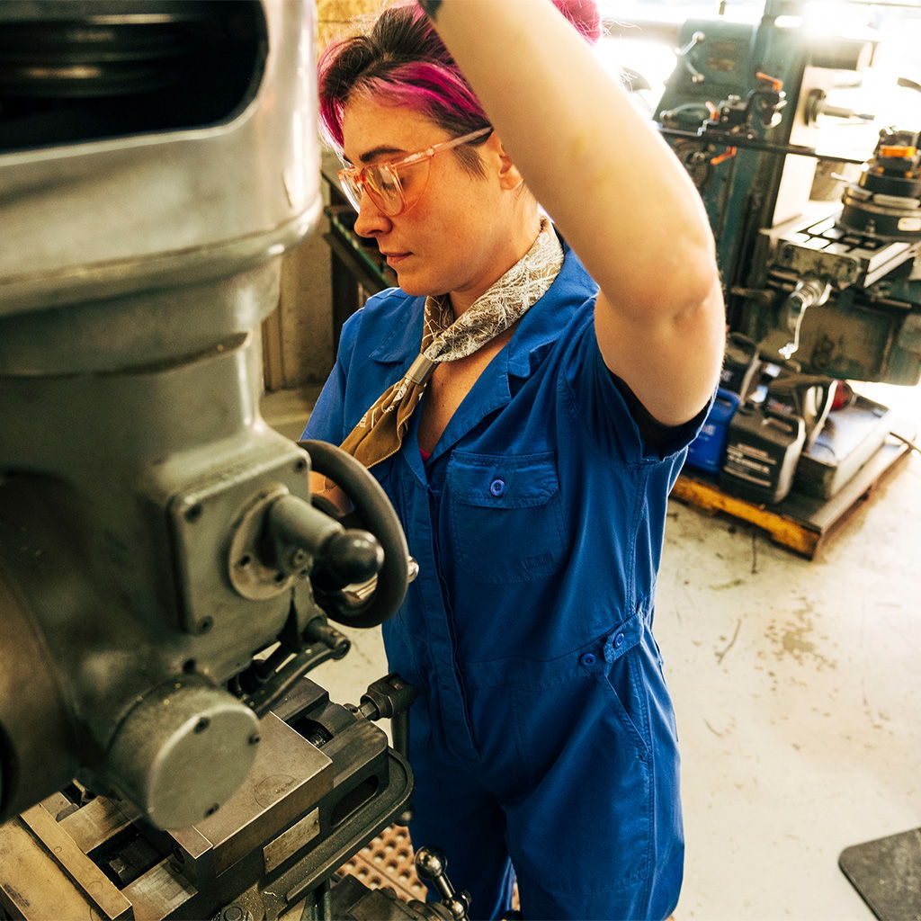 Person in blue jumpsuit working on machinery in a workshop.