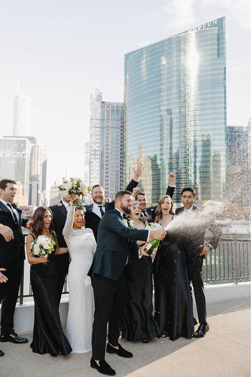 Wedding party celebrating with champagne in front of city skyline.