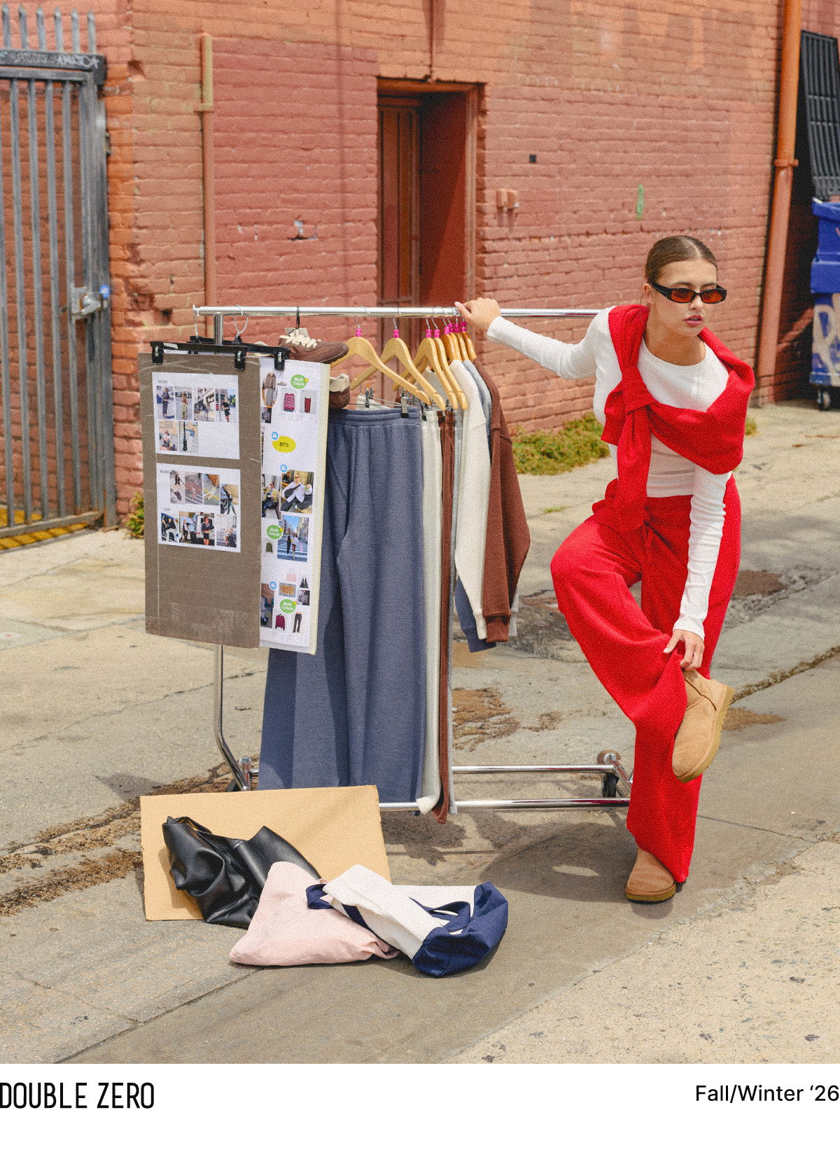 Model in red outfit poses near clothing rack in urban setting.