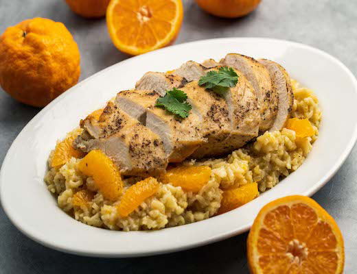 Sliced chicken on rice with tangerine segments and garnished with herbs.