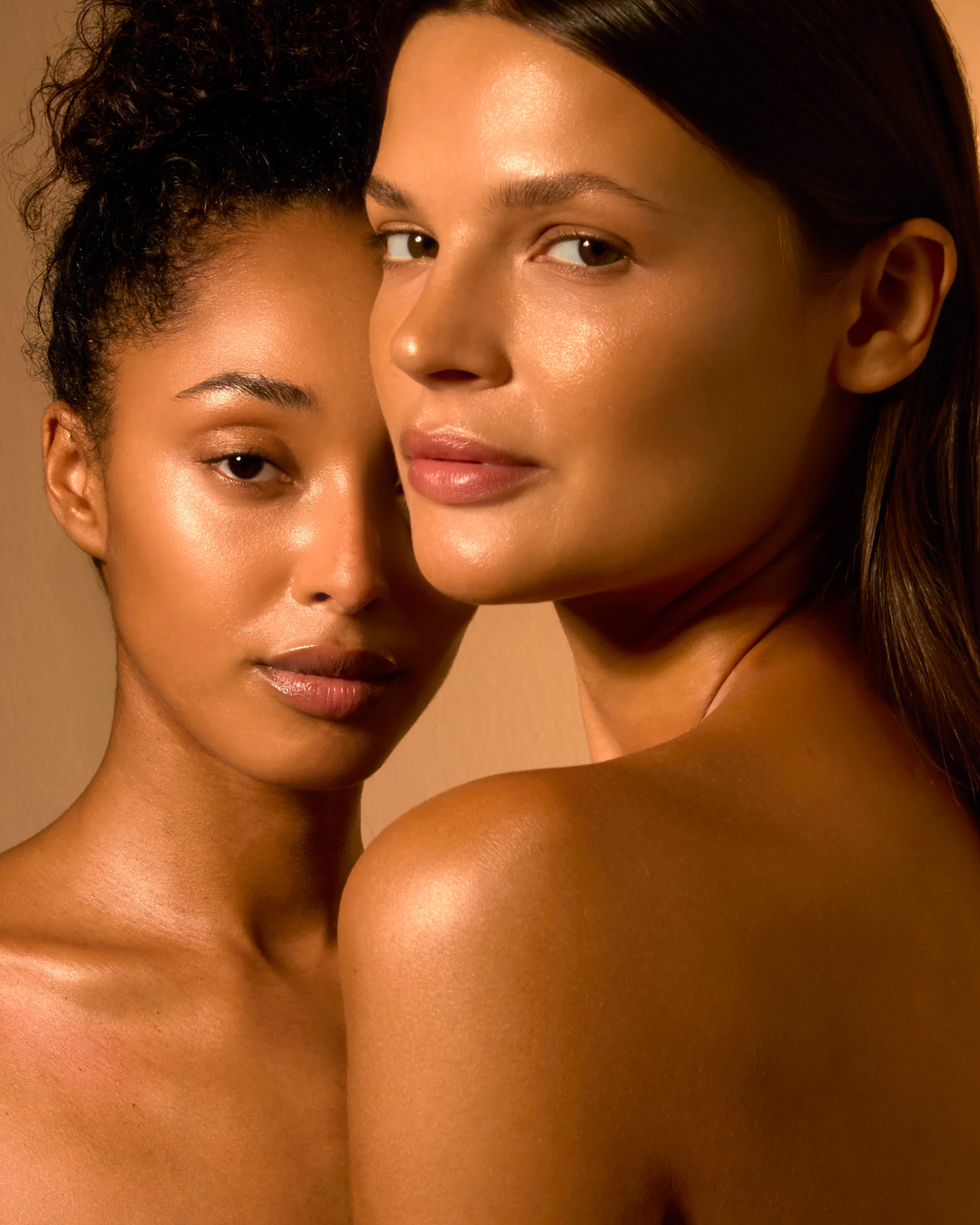 Two women with natural makeup, posing closely together, facing the camera.