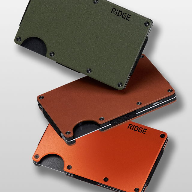 Three Ridge wallets in green, orange, and black stacked on a gray background.