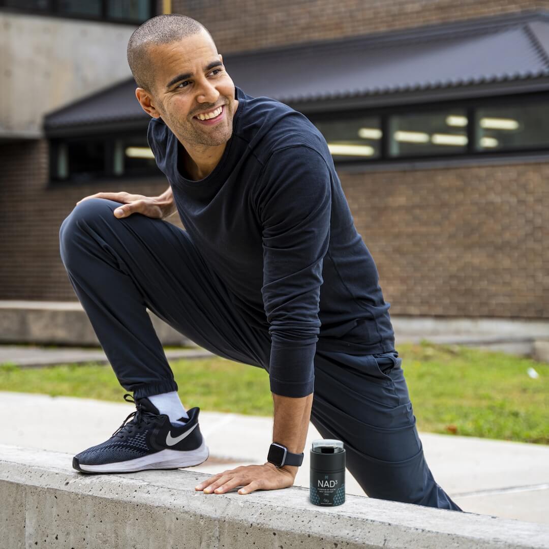 Man stretching outdoors, wearing athletic clothing, with a speaker beside him.