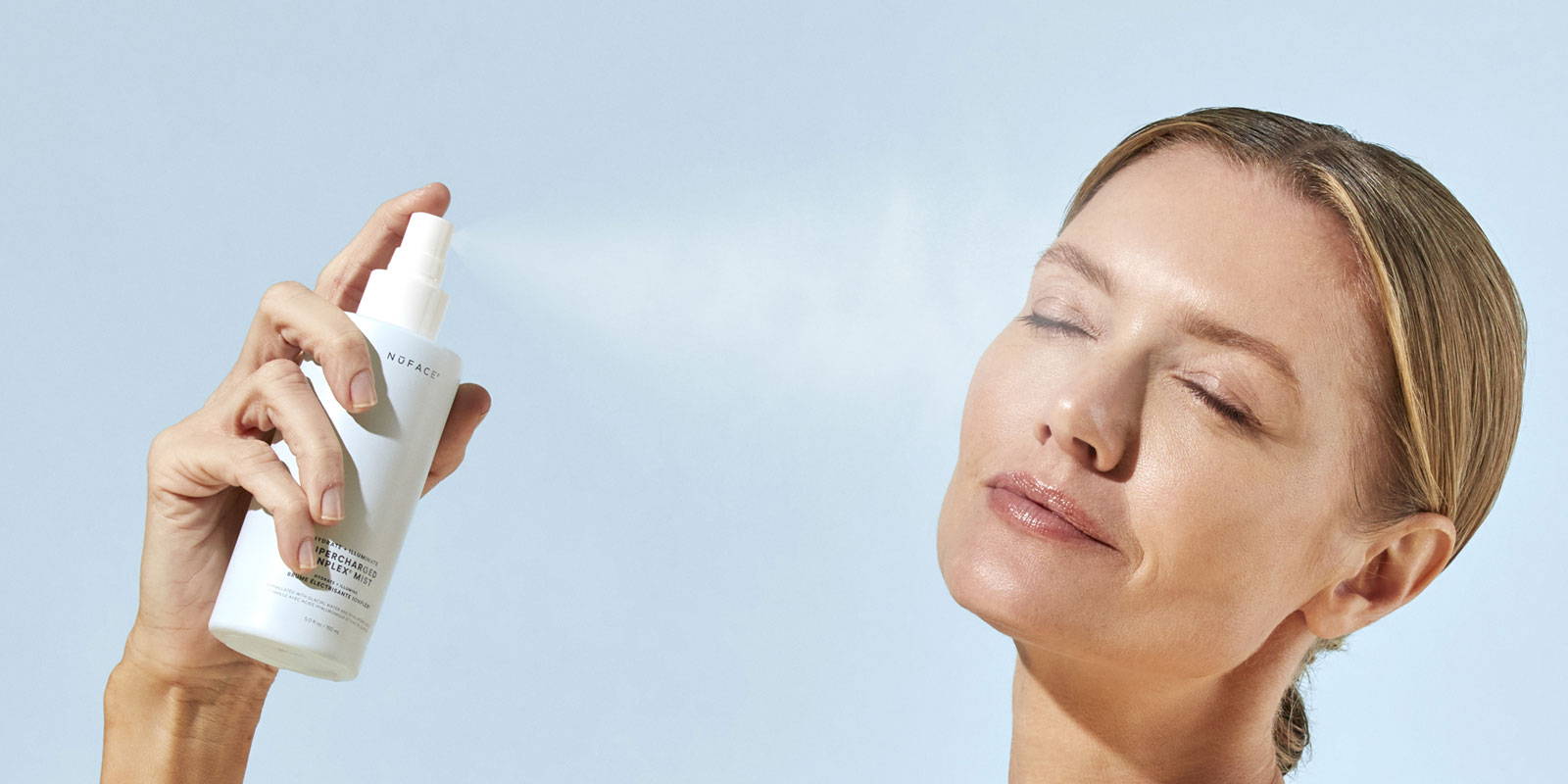 a photo of a happy NuFACE woman spraying Supercharged IonPlex® Facial Mist onto her face