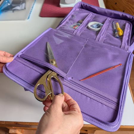 women grabbing golden shears out of a purple zipper binder bag holding other tools