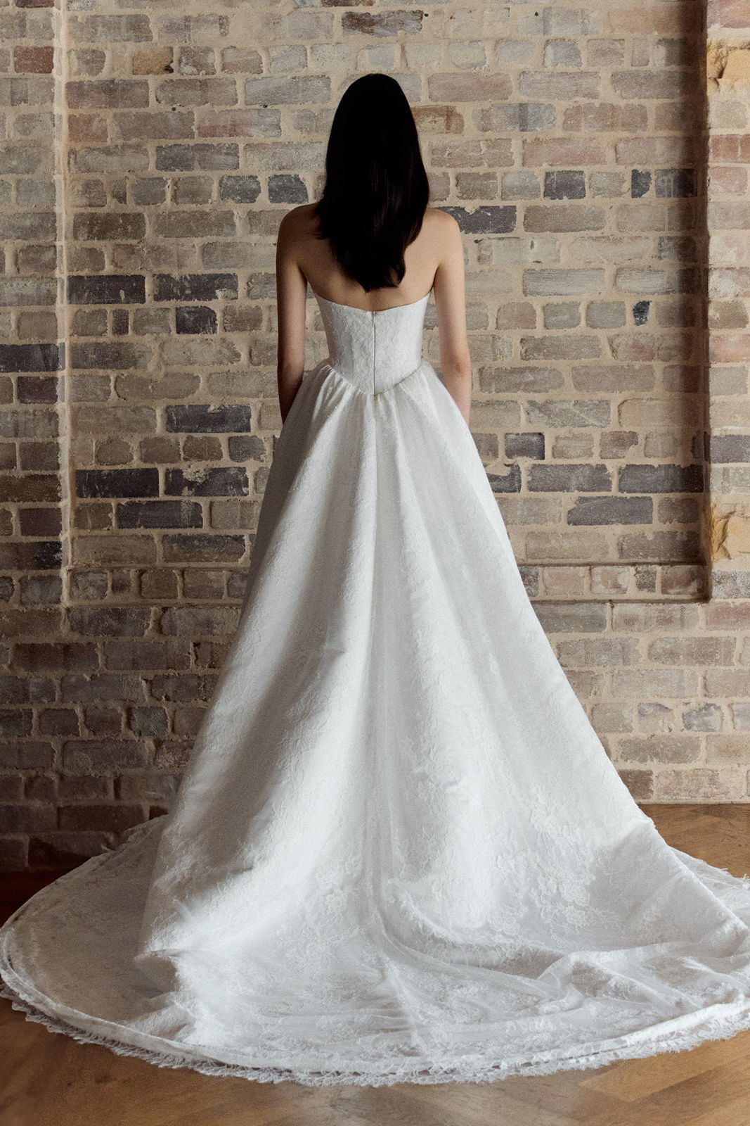 Woman in a white wedding dress standing against a brick wall.