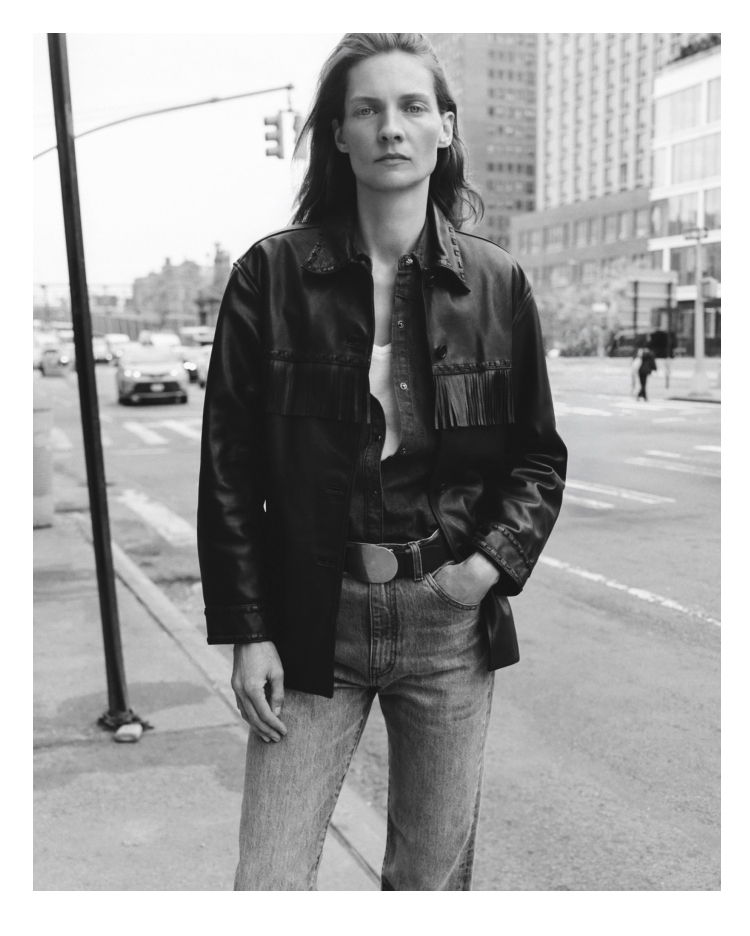 Model wearing a black leather jacket and jeans in an urban setting.