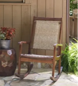 A wooden rocking chairs sits on a front porch in the summer sun.