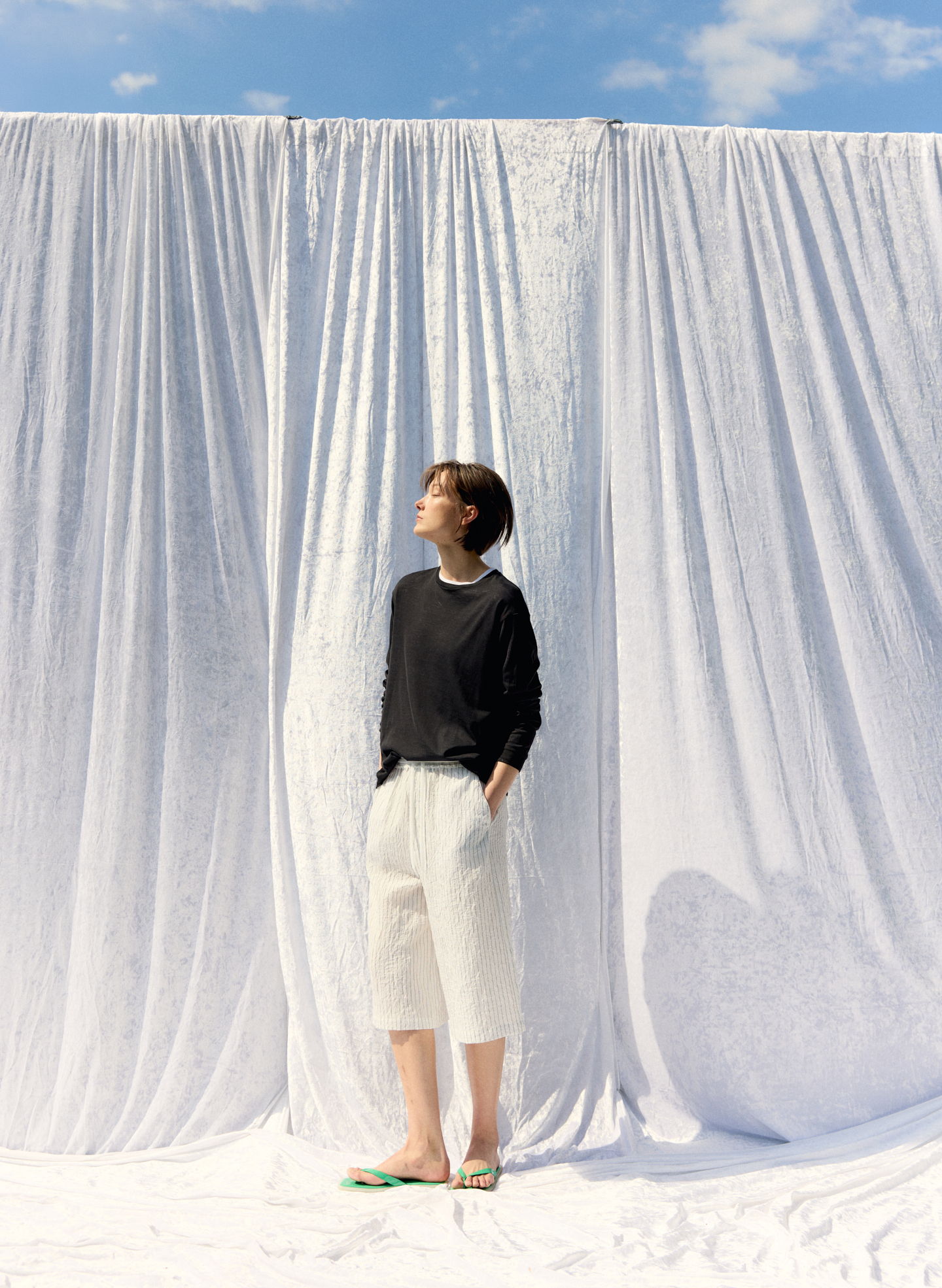 Person standing in front of white drapes against a blue sky.
