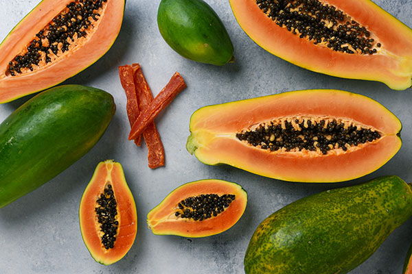 Sliced and whole papayas with green fruit and strips of dried fruit.