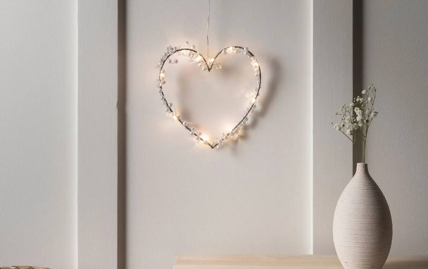 Beaded heart light in a cosy room with a delicate flower in a vase.