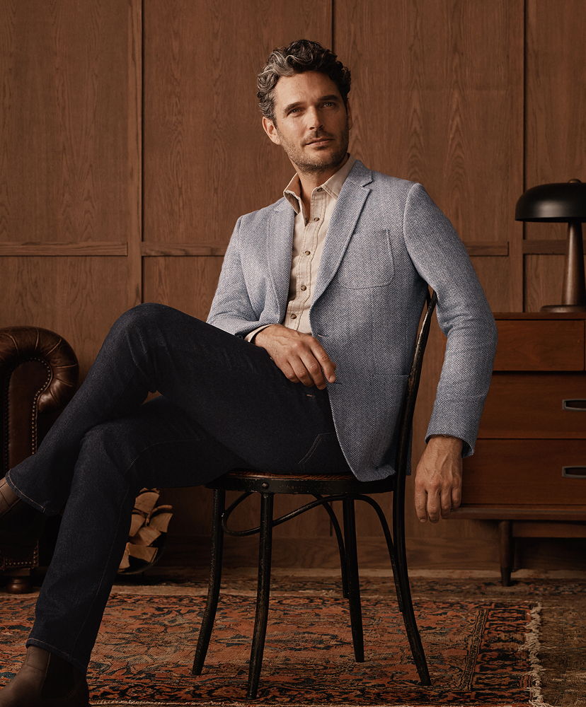 Man sitting on a chair wearing a light blazer and button-up shirt.
