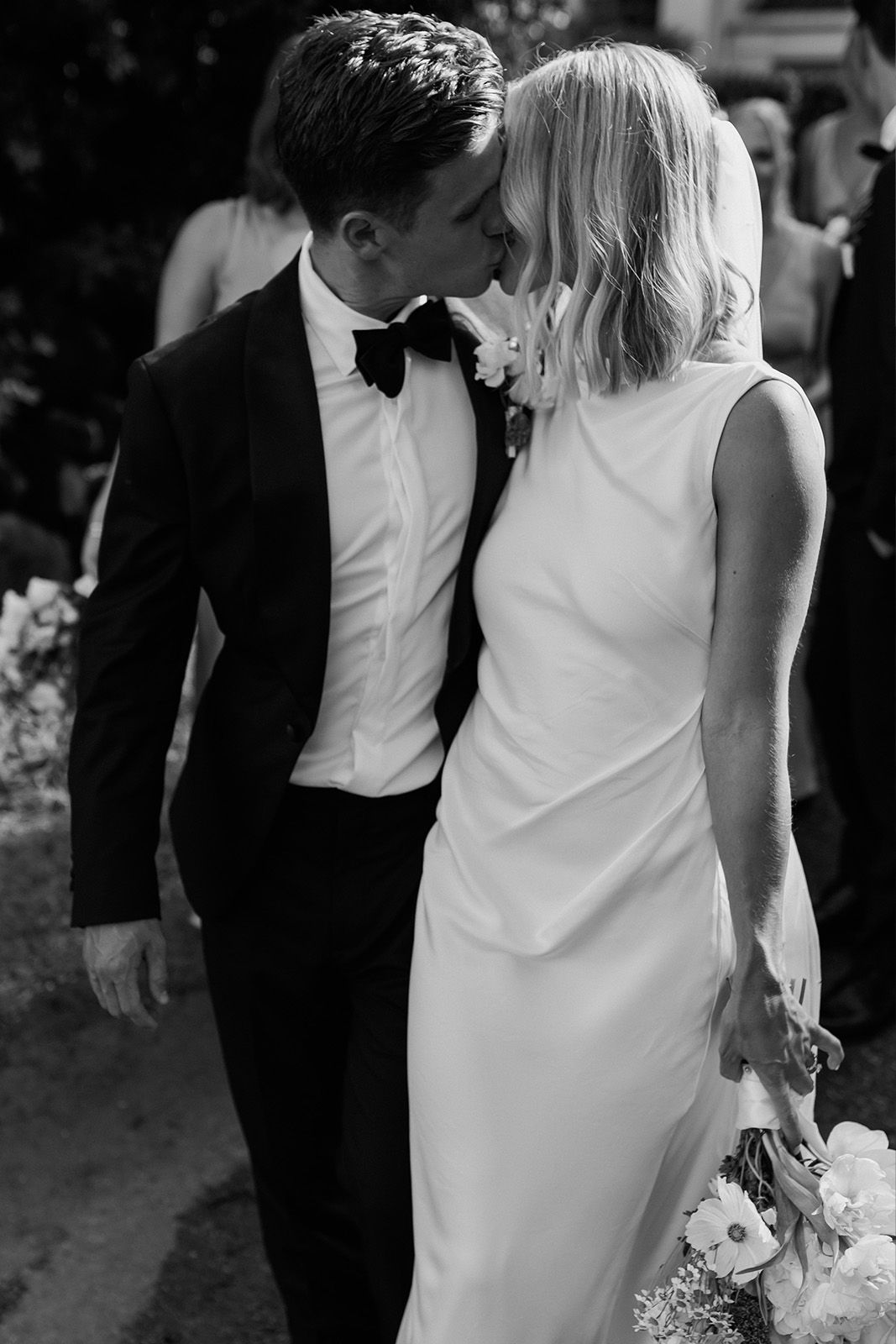A couple shares a kiss at their wedding, dressed elegantly.