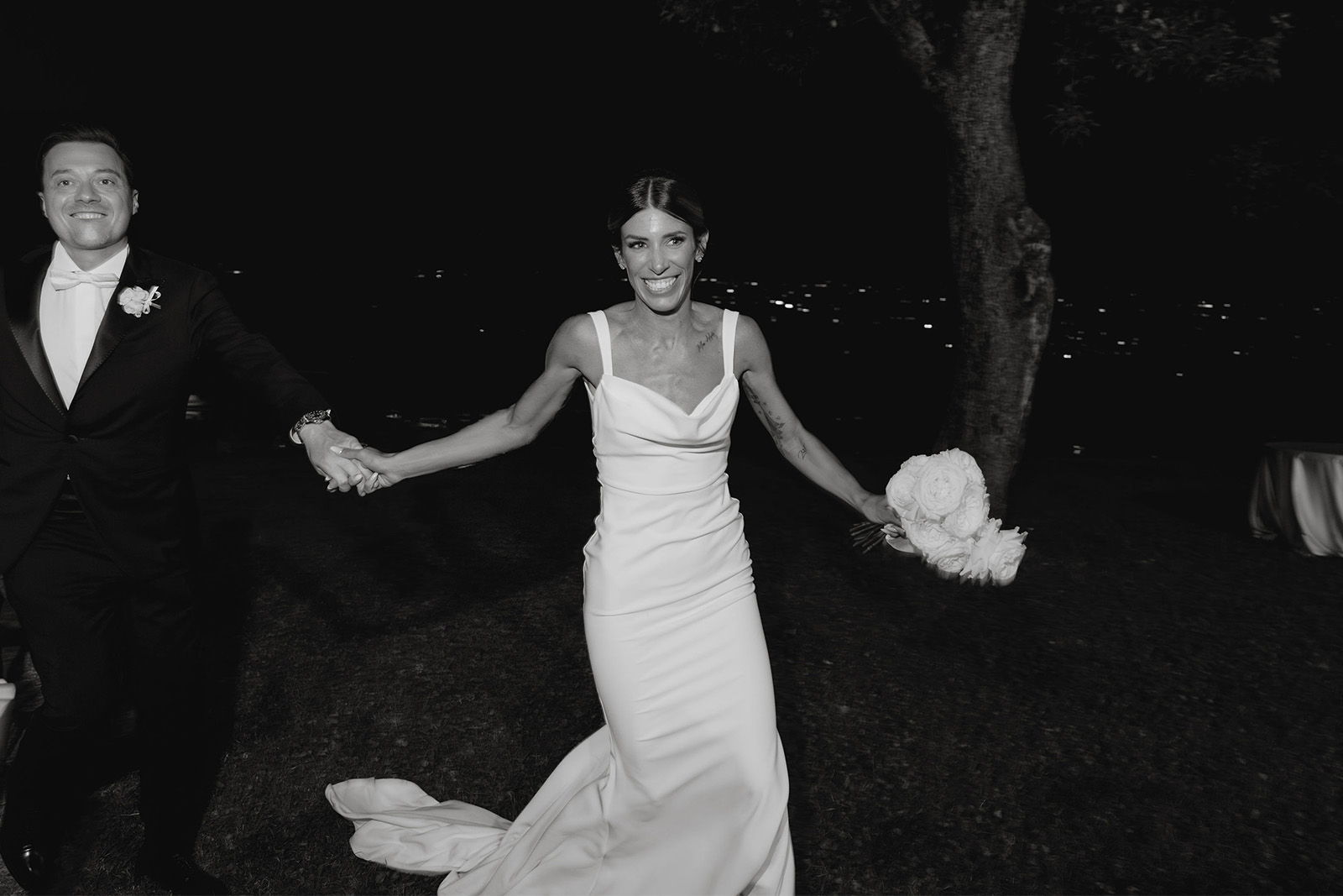 Bride and groom joyfully walking together at night, holding hands.