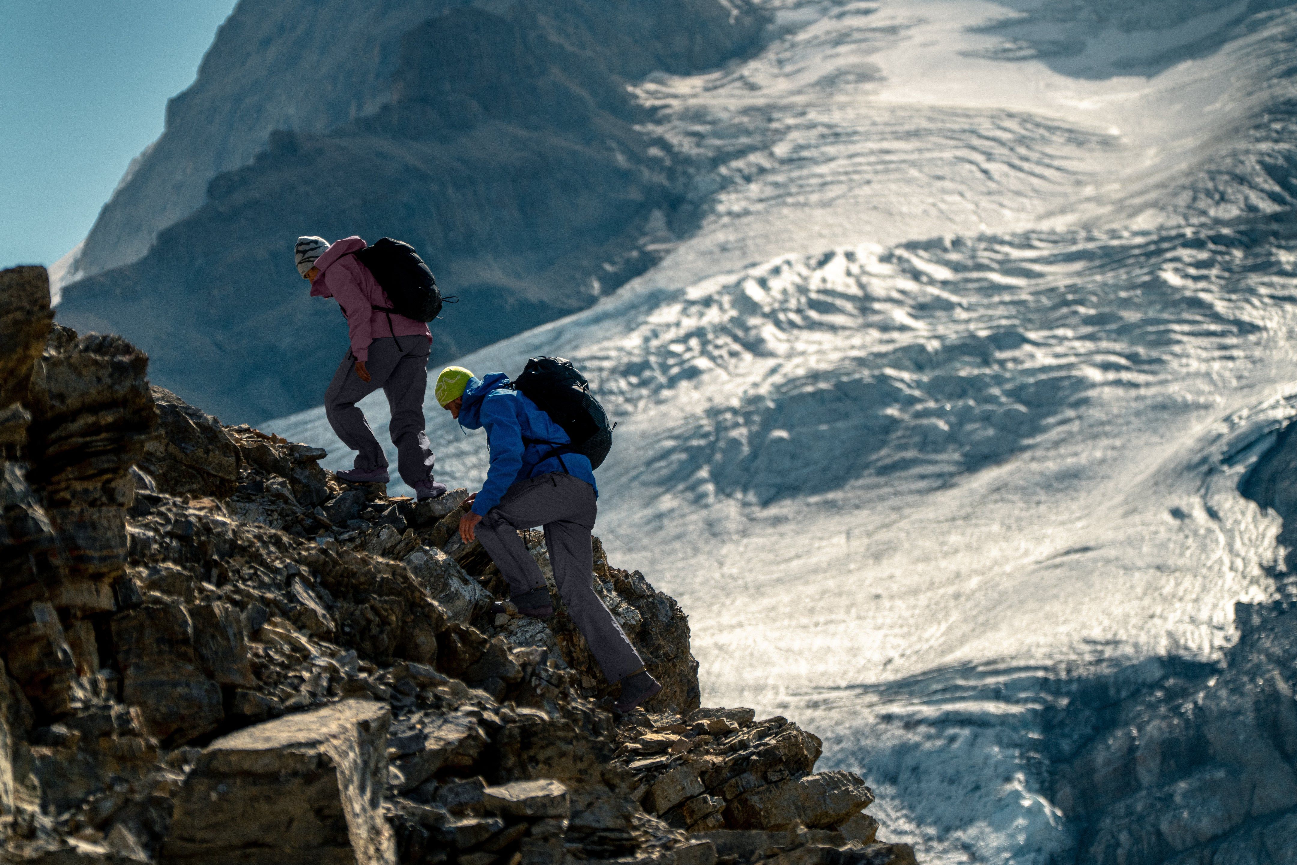 Two climbers ascending rocky terrain with a glacier in the background.
